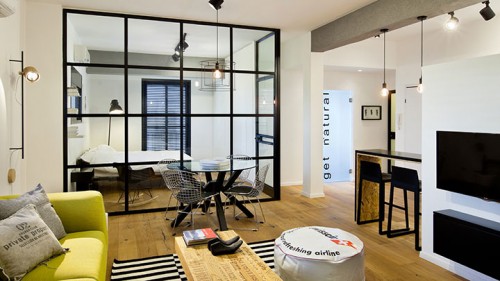 קיר זכוכית שקוף שמוסגר בריבועי אלומיניום שחורים מפריד בין חדר השינה לסלון, ומחליף את הקיר העבה ומלא הנישות שעמד במקום. צילום: בועז לביא  