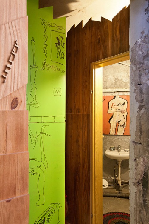 הצצה אל חדר הרחצה דרך משקוף דלת רחב מעץ בעיצובו של רזגור. מאחוריו - משטח ירוק עז שישמש כמצע לרישום בטוש. צילום: בועז לביא