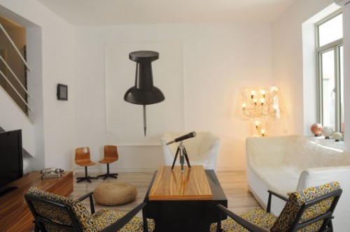 רישום ענק של אירינה בירגר, המגדילה לממדי ענק חפצים יומיומיים קטנים, נתלה על קיר מרכזי בסלון. על הקיר הניצב נתלתה עבודת וידיאו של צמד אמני המיצג " בית הזכוכית". צילום: סוזי לוינזון