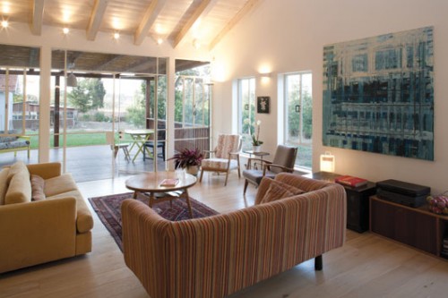 ציור שמן גדול של עופרי מירום וציור קטן של ארן זינגר, משתלבים עם אוסף רהיטי יד שנייה בסלון של בית במושב. צילום: בועז לביא