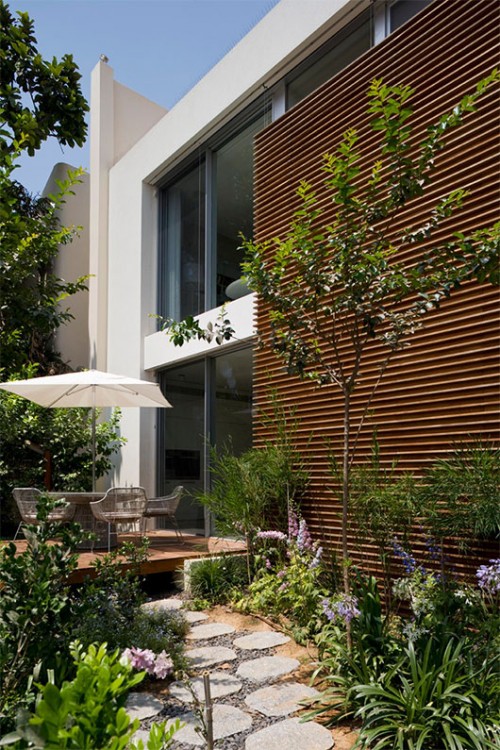 קיר מרשים בצורת רי"ש מקיף את חזית הבית. הוא חופה בקורות עץ אופקיות המוסיפות לבית חמימות ותורמות לתחושה שהקיר ארוך ממידותיו | צילום: אורי אקרמן ומיקלה ברסטו