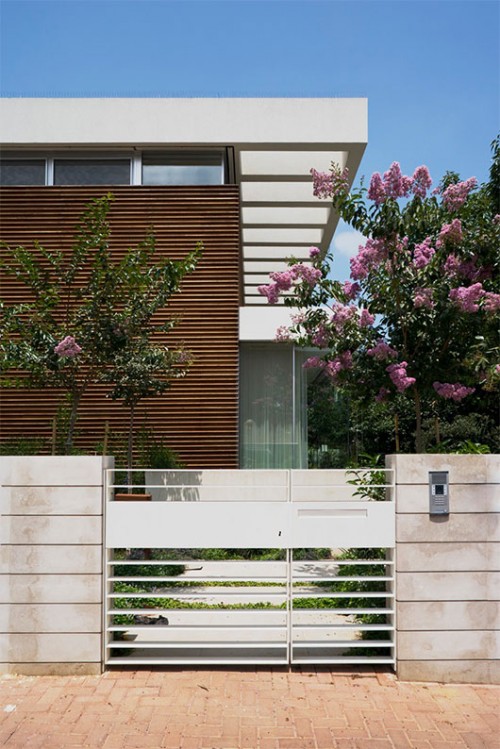 קיר מרשים בצורת רי"ש מקיף את חזית הבית. הוא חופה בקורות עץ אופקיות המוסיפות לבית חמימות ותורמות לתחושה שהקיר ארוך ממידותיו | צילום: אורי אקרמן ומיקלה ברסטו