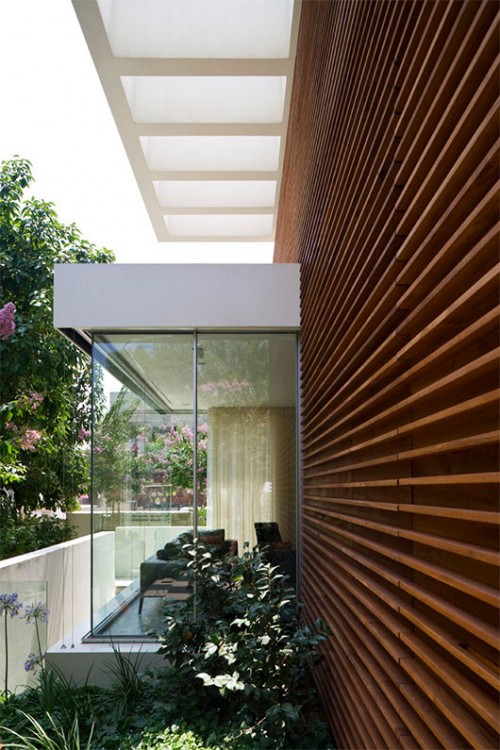 קיר מרשים בצורת רי"ש מקיף את חזית הבית. הוא חופה בקורות עץ אופקיות המוסיפות לבית חמימות ותורמות לתחושה שהקיר ארוך ממידותיו | צילום: אורי אקרמן ומיקלה ברסטו