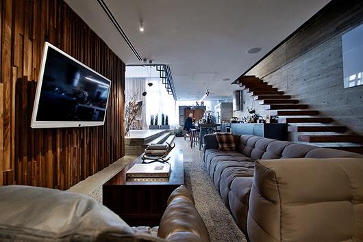 קיר פינת הישיבה לצד המטבח, העשוי כפיסי עץ (אשד נגרים), נבחר כדי ליצור ניגוד לקרירות ולמנימליזם של הבטון והברזל, והוא הקו המחבר אל הקומה הפרטית, שם הוא משמש כקיר חדר השינה | צילום: איתי סיקולסקי