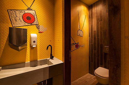 אריחים דמויי פרקט וקירות צהובים עם ציורים בסגנון אמנות רחוב מחברים את השירותים אל החלל המרכזי | צילום: ינאי דיטש