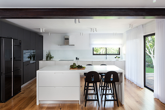 מבט אל המטבח מהסלון: קורת ברזל חשופה הותקנה במקום עמוד שהוסר ומשמשת אלמנט מבני ועיצובי | צילום: טל ניסים