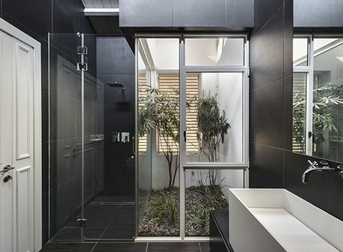 פטיו צר הפתוח לשמים מחדיר לחדר הרחצה אור יום רב וגם גשם בחורף המתדפק על קירות הזכוכית של המקלחון | צילום: עודד סמדר