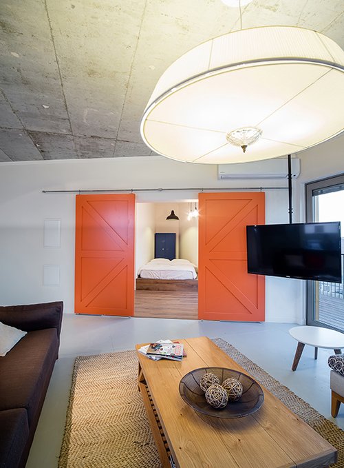 דלתות עץ מאסיביות שנצבעו בכתום עז בדירת לופט ביפו, ניתנות להזזה על צינור ברזל באופן המאפשר לייצר הפרדה בין הסלון לחדר השינה | צילום: חפצי אלגר